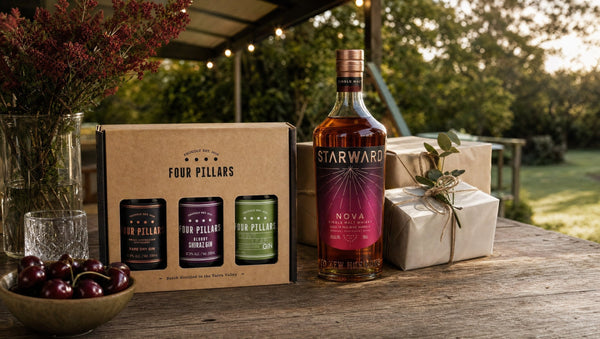 Four Pillars Gin Gift Pack and Starward Nova single malt beside wrapped gifts on a veranda table in summer, with NSW Christmas bush and cherries