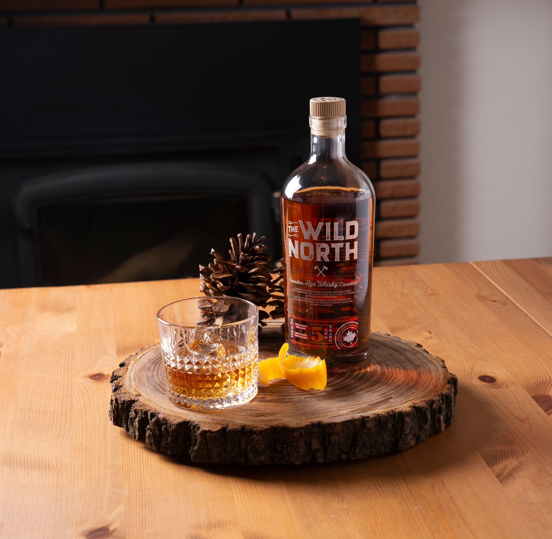 A photo of sortilege whisky on a wooden plate, with a glass of whisky. The whiskey is on a table with a fireplace in the background